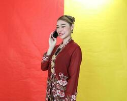 ásia mulher tradicional marrom kebaya sharong em vermelho amarelo papel fundo conversa usar telefone Smartphone foto