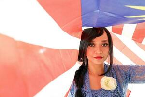 sul leste ásia malaio raça étnico origem mulher vestindo azul kebaya vestir traje compartilhar multirracial comunidade segurando debaixo malaio bandeira jalur gemilang em branco fundo foto