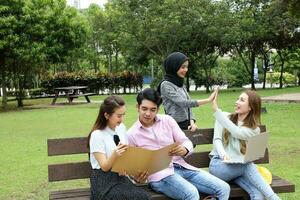 jovem ásia malaio chinês homem mulher ao ar livre em parque Banco estude conversa discutir ponto computador portátil Arquivo livro foto
