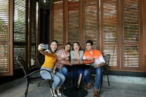 grupo jovem ásia malaio homem mulher às rústico de madeira cafeteria mesa Conheça conversa discutir o negócio estude selfie auto retrato mão inteligente telefone foto