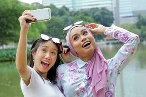 dois mulher malaio chinês indiano ásia malaio ao ar livre verde parque lago natureza selfie Smartphone Câmera auto retrato foto