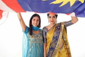 dois sul leste ásia indiano raça étnico origem mulher vestindo indiano vestir traje compartilhar e salwar kameez multirracial comunidade segurando debaixo malaio bandeira jalur gemilang em branco fundo foto