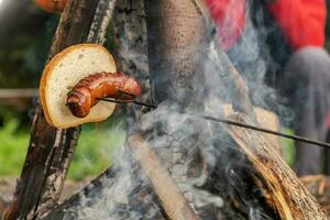 queimando polonês linguiça e peça do branco pão em uma fogueira foto