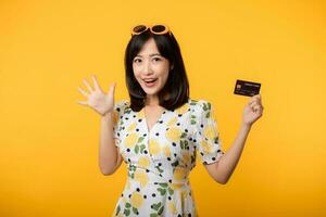 retrato jovem ásia mulher feliz sorridente dentro primavera vestir mostrando plástico crédito cartão isolado em amarelo fundo. pagar, dinheiro e compra compras Forma de pagamento conceito. foto