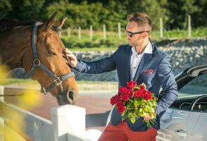 bonito homem com ramalhete do vermelho rosas acariciando cavalo. foto