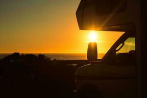 campista furgão motor casa dentro frente do a mar durante pôr do sol foto