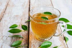 xícara de chá e folhas de chá frescas em uma mesa de madeira foto