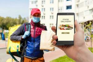 Entrega Comida serviço às lar. homem correio entregue a ordem não nome saco com Comida. mão segurando inteligente telefone com Comida conectados dispositivo em tela foto