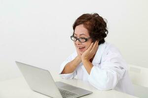 idosos ásia chinês fêmea médico em branco fundo vestindo branco avental caderno computador mão em bochecha feliz foto