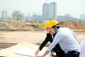 homem mulher malaio chinês trabalhador engenheiro gestão Difícil segurança chapéu capacete às construção local lendo vendo plano foto