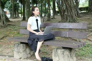 jovem ásia chinês mulher ao ar livre em parque Banco usar computador portátil computador pensar ler Veja feliz maravilha foto