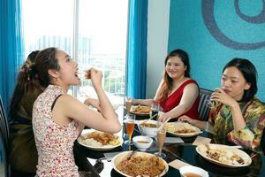 jovem sudeste ásia mulher grupo conversa comemoro comendo desfrutando Comida arroz Curry macarrão frango beber Felicidades em jantar mesa foto