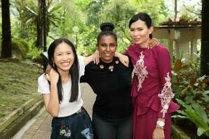 três mulher malaio chinês indiano ásia ao ar livre verde parque andar conversa misturar-se feliz alegria foto