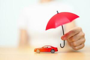 mão de empresária segurando o guarda-chuva vermelho e cobrir o brinquedo do carro vermelho na mesa. seguro de carro, garantia, reparo, financeiro, bancário e conceito de dinheiro foto