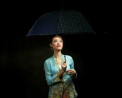 ásia mulher dentro tracional kebaya carregando guarda-chuva em Preto fundo foto