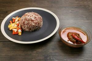 nasi maldito especial Castanho branco arroz cozinhou com coco leite em conserva fruta vegetal abacaxi cenoura em Preto fora branco aro prato peixe Curry dentro tigela sobre rústico Sombrio de madeira fundo foto