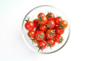 vermelho maduro cereja tomate com haste vidro tigela em branco fundo topo Visão foto