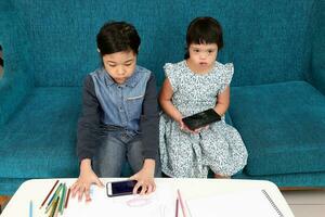 dois pequeno sul leste ásia menina criança malaio chinês estude jogar desenhar usar inteligente telefone em azul tecido sofá elas estão autista e baixa síndrome foto