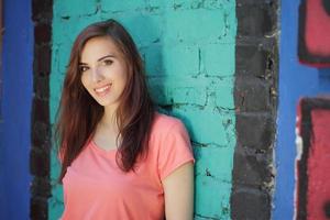 garota sorridente com cabelo castanho perto de uma parede colorida foto
