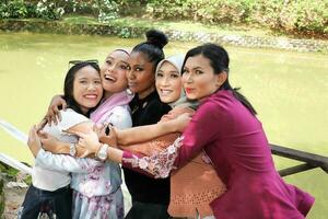 grupo do cinco mulher amigos malaio chinês indiano ásia ao ar livre parque lago natureza abraçando carinhoso rindo feliz foto