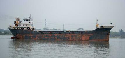 velho e oxidado carga navio cheio corpo lado visualizar. água transporte e logística conceito. carga navio com oxidado metal âncoras indo através uma rio. velho via fluvial embarcação e petroleiro navio em uma rio. foto