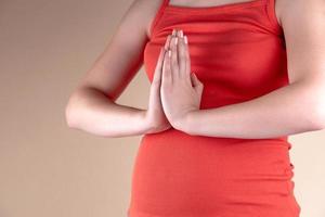 uma visão aproximada da barriga de uma mulher grávida em uma camiseta vermelha com os braços cruzados para orar