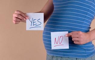 uma visão aproximada da barriga de uma mulher grávida em uma camiseta azul segurando dois lençóis com as palavras sim e não foto