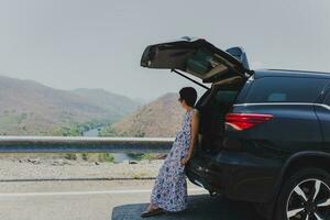 relaxado turista mulher inclinado novamente carro com aberto porta-malas. foto