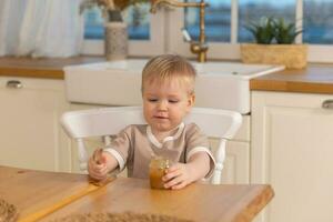 feliz família às lar. bebê Garoto alimentando ele mesmo dentro cozinha. pequeno Garoto com bagunçado engraçado face come saudável Comida. criança aprende comer de ele mesmo segurando colher. auto alimentando. foto