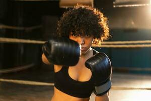 mulheres auto defesa poder. africano americano mulher lutador soco com boxe luvas para Câmera. saudável Forte menina soco Treinamento socos olhando concentrado direto. em forma corpo dar certo. foto