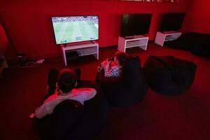 dois Rapazes gamers jogar futebol controle vídeo jogos console dentro vermelho jogos sala. foto