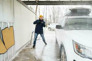 homem lavando carro suv americano de água de alta pressão com rack de teto na lavagem de autoatendimento em clima frio. foto