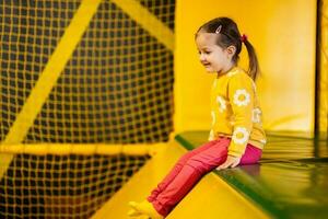 bebê menina criança deslizar às amarelo Parque infantil parque. criança dentro ativo entretenimento. foto