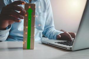 homem segurando um cubo com uma seta verde na mesa com o computador foto