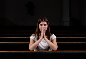 uma menina cristã de camisa branca está orando com o coração humilde na igreja foto