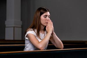 uma menina cristã de camisa branca está orando com o coração humilde na igreja foto