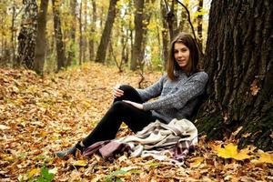 linda garota com uma jaqueta cinza sentada na floresta de outono foto