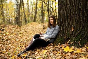 linda jovem com uma jaqueta cinza sentada na floresta de outono foto