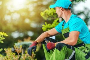 profissional jardineiro sentado dentro a jardim com poda tesoura de jardim dentro mão foto