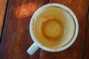 topo Visão sobras café com espuma dentro uma branco cerâmico caneca em Castanho de madeira chão fundo, objeto, comida, bebida, cópia de espaço foto