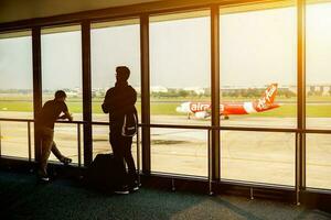 Bangkok, tailândia, 2018- turista homens esperando para a ar avião dentro a aeroporto terminal lobby com Sol flare e vermelho ar avião do ar Ásia CIA aérea em pista fundo. foto