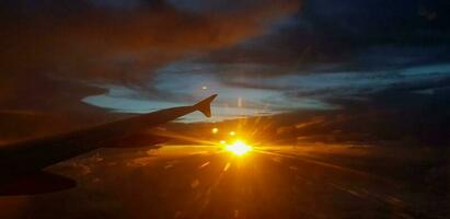silhueta do aeronave ou avião asa em Sombrio céu com pôr do sol luz flare fundo. transporte, viagem e beleza do natureza conceito foto