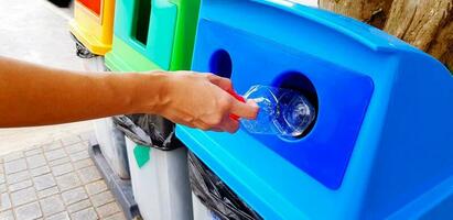 fechar acima mulher mão segurando e dumping plástico garrafa do água para dentro azul reciclar bin, lixeira ou lixo. limpeza área e reciclando usava com cópia de espaço. foto