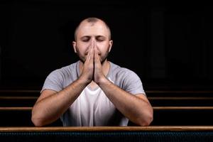 um homem cristão de camisa branca está sentado e orando com o coração humilde na igreja foto