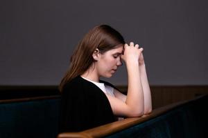 uma menina cristã de camisa branca está sentada e orando com o coração humilde na igreja