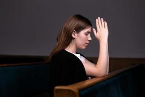 uma menina cristã de camisa branca está sentada e orando com o coração humilde na igreja