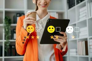 conceito de avaliação de serviço ao cliente. empresária pressionando rosto sorriso emoticon show na tela virtual no tablet e smartphone no escritório foto