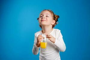 retrato do uma pequeno menina do eslavo aparência bebendo laranja suco em uma azul fundo foto