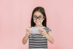 pequeno menina jogar telefone móvel. isolado em Rosa fundo foto