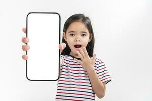 ásia pequeno menina segurando Smartphone brincar do em branco tela e sorridente em branco fundo. foto